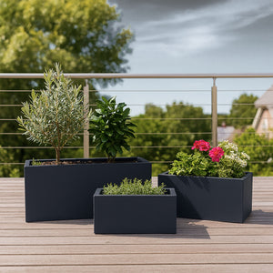 Moderne terrasse med tre svarte blomsterkasser fylt med urter, blomster og små trær – perfekt for stilfull dyrking på balkong eller platting