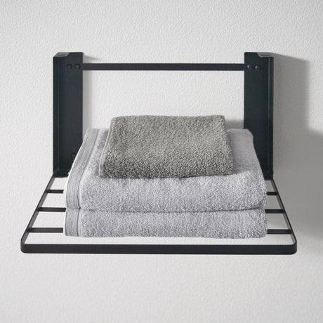 Vegghengt hylle i sort metall for håndklær og oppbevaring.