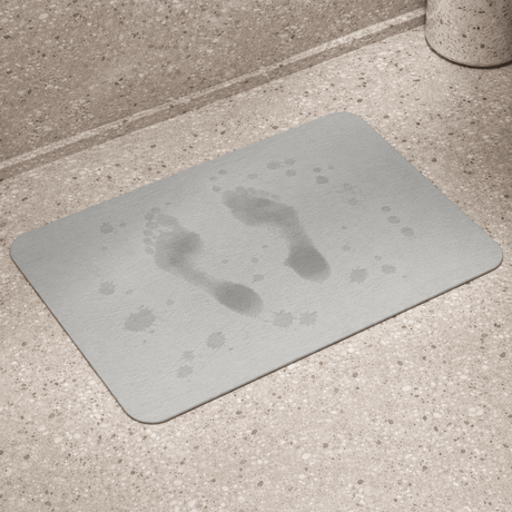Grå baderomsmatte i diatomitt med våte fotavtrykk på overflaten