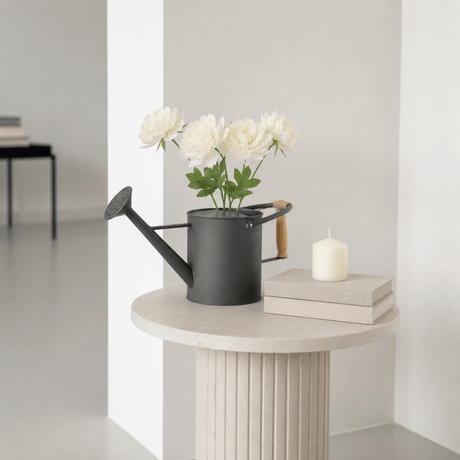 Mørk grå dekorativ vannkanne brukt som vase med hvite blomster på et rundt pyntebord i et lyst, nordisk interiør. - Lindas dekor 