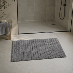 Grå Tiles baderomsmatte foran en dusj med glassvegg i et moderne baderom. - Lindas dekor