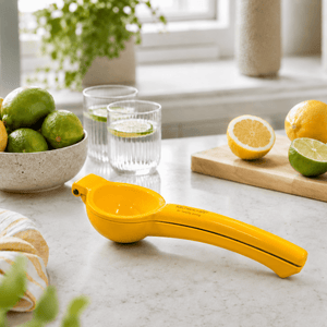 Gul KitchenCraft-sitronpresse på en lys kjøkkenbenk med sitroner, lime og glass i bakgrunnen. - Lindas dekor 
