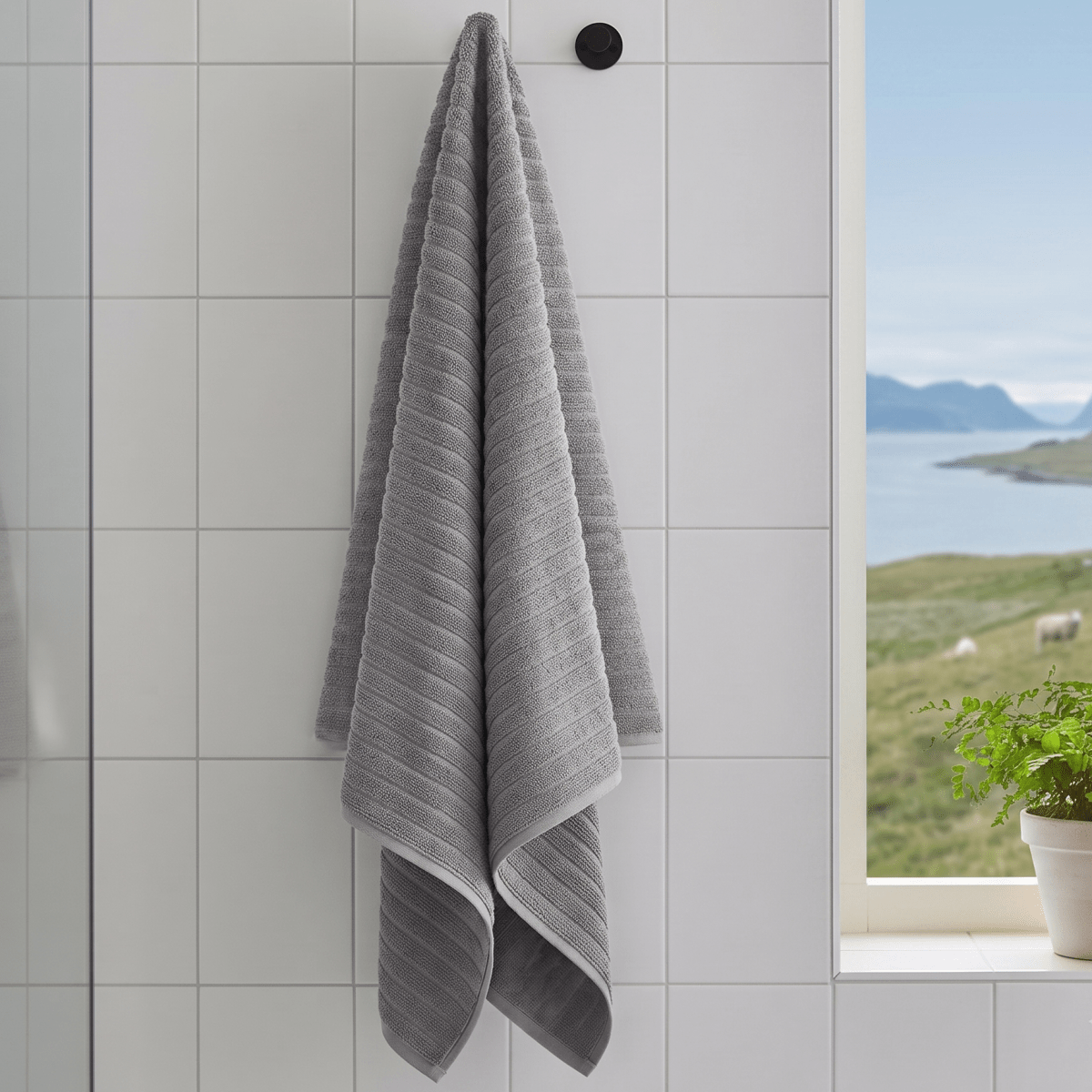 Grått Inu badehåndkle hengende på krok ved vindu i lyst baderom med moderne uttrykk.