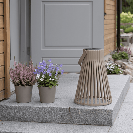 Brun solarlykt plassert på en hellelagt uteplass ved blomsterpotter og grønne planter. - Lindas dekor