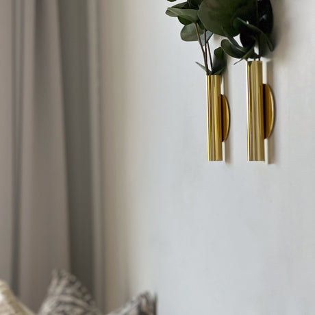 Liten vegghengt metallvase med eucalyptus kvister på lys vegg