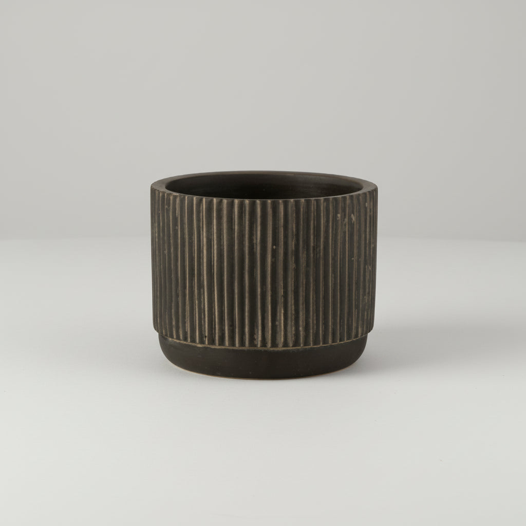 Detaljbilde av liten keramikkpotte med stripet design i svart og brune toner
