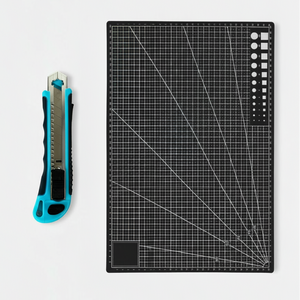 Skjærematte A3 30 x 45 cm sort med utstyrskniv i bruk til å kutte kontaktplast på lyst arbeidsbord.

