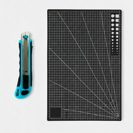 Skjærematte A3 30 x 45 cm sort med utstyrskniv i bruk til å kutte kontaktplast på lyst arbeidsbord.

