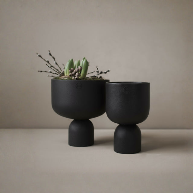 DBKD Post potte sort liten fra Lindas Dekor med grønn plante mot lys 