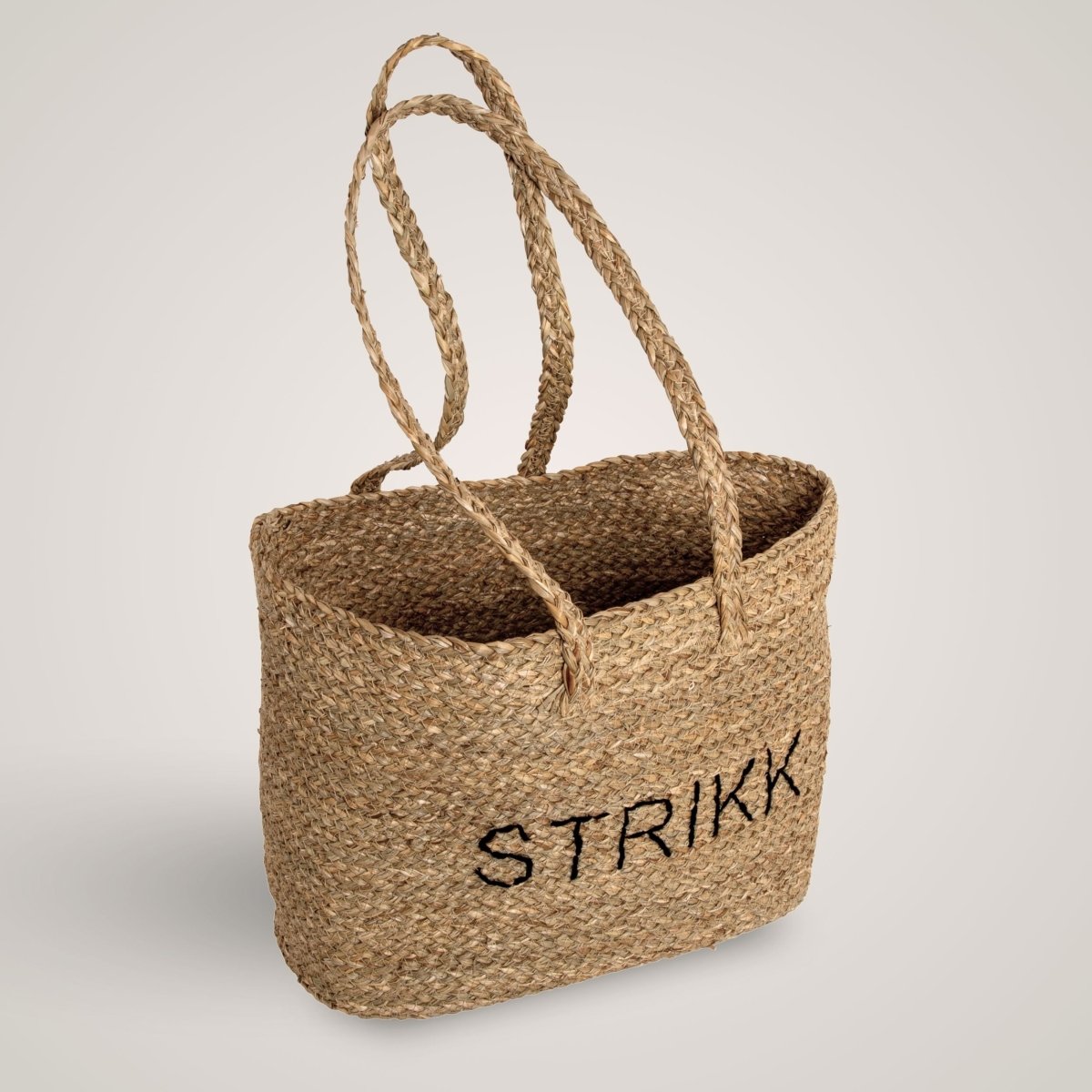 Håndlavet stråveske med teksten STRIKK, to flettede hænkler og en naturlig tekstur. Perfekt til hobby og opbevaring.