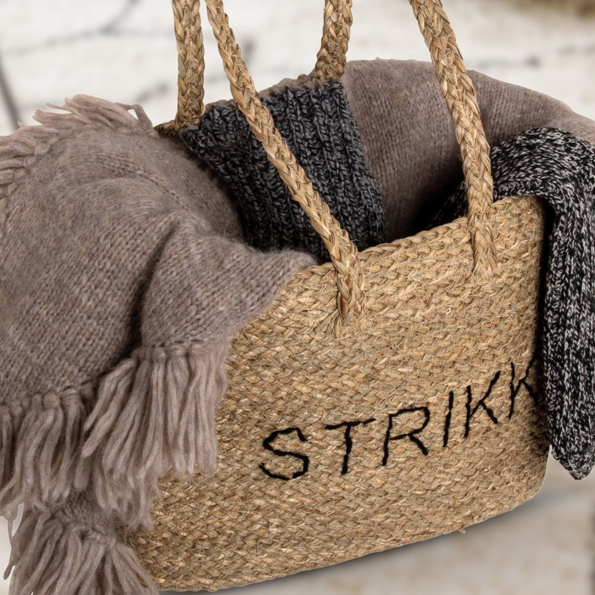 Strikkepose med teksten STRIKK fyldt med uldskeier og strikkeprojekter i varme, neutrale toner.