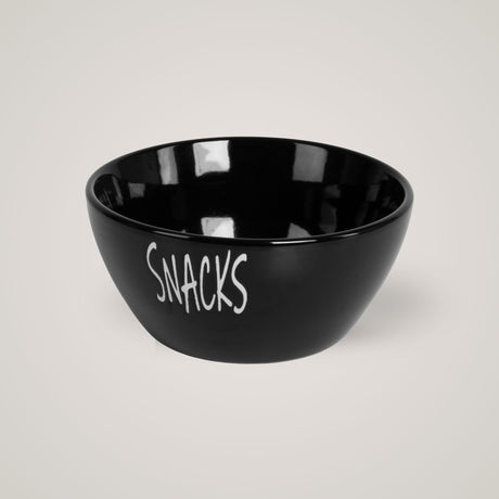 Sort snacks-skål med hvit tekst, plassert mot lys beige bakgrunn.