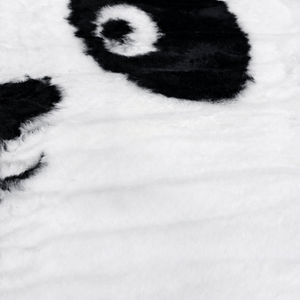Nærbilde av mykt pandateppe i svart og hvitt med fluffy overflate i polyester, designet som et pandaansikt til barnerom.