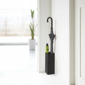 Sort paraplyholder i stål plassert i hjørne ved inngangsparti