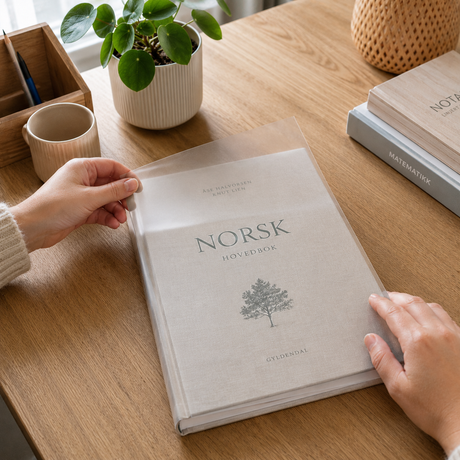 Norsk skolebok med transparent matt kontaktplast på omslaget i lyst hjemmemiljø.