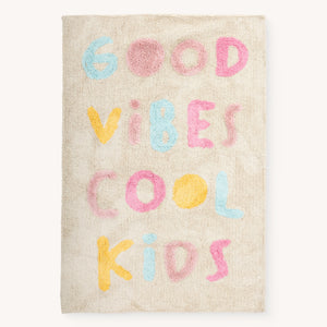 Tuftet barneteppe i bomull med Good Vibes Cool Kids tekst i pastellfarger, vist rett ovenfra