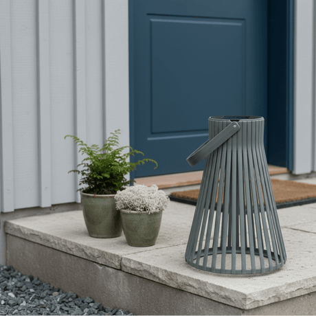Grønn solarlykt plassert ved et moderne inngangsparti med svart ytterdør, grå vegg og grønne planter i potter. - Lindas dekor 