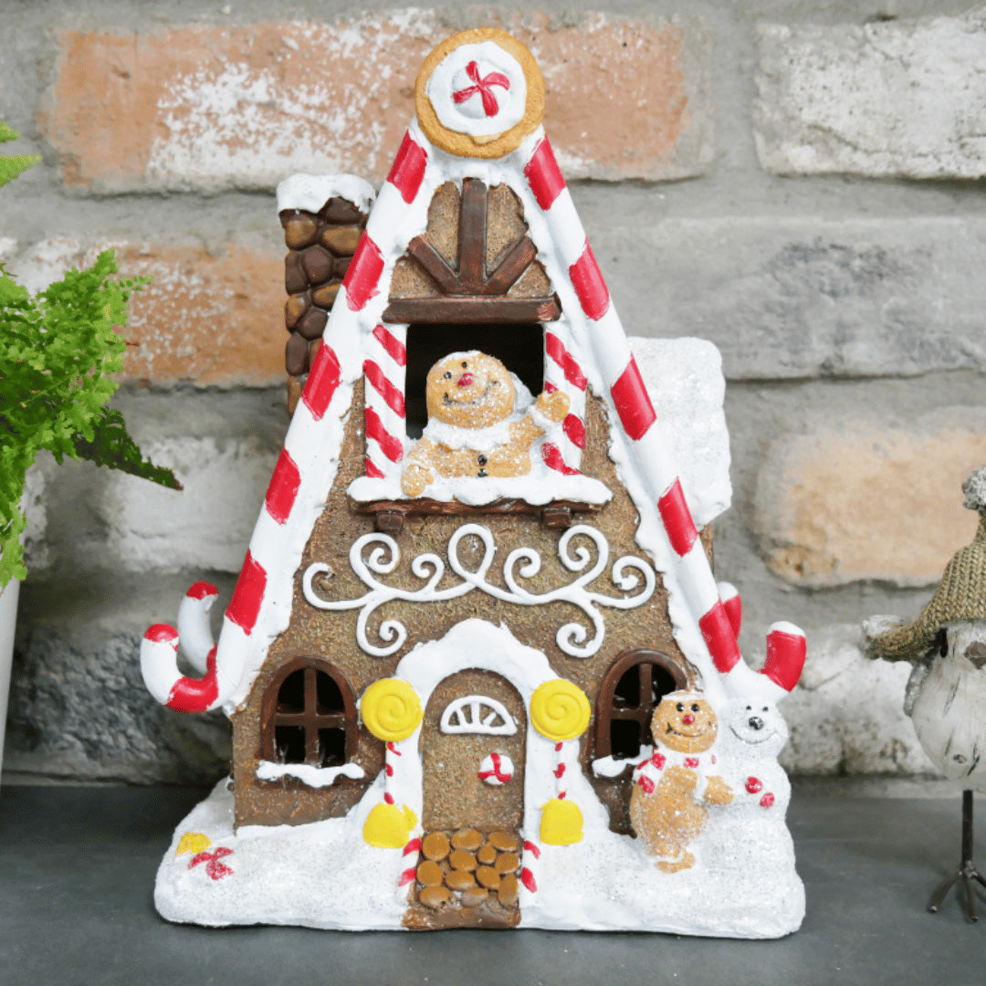 Pepperkakehus med juledekor mot mursteinsbakgrunn, pyntet med sukkerrør, glasur og pepperkakefigurer.