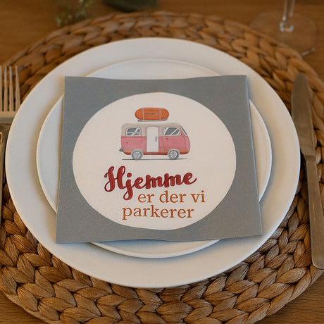 Serviett med campingmotiv og teksten «Hjemme er der vi parkerer» – perfekt til borddekking i bobil, campingvogn eller sommermiddag.