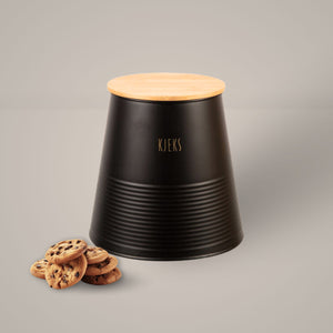 Sort metallboks med bambuslokk og gulltekst «Kjeks», plassert på kjøkkenbenk med kjeks ved siden av.