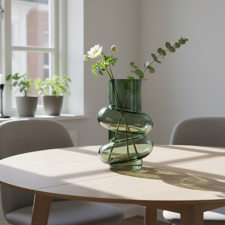 Vase flaskegrønn glass 16 cm med grønt på bord naturlig lys
